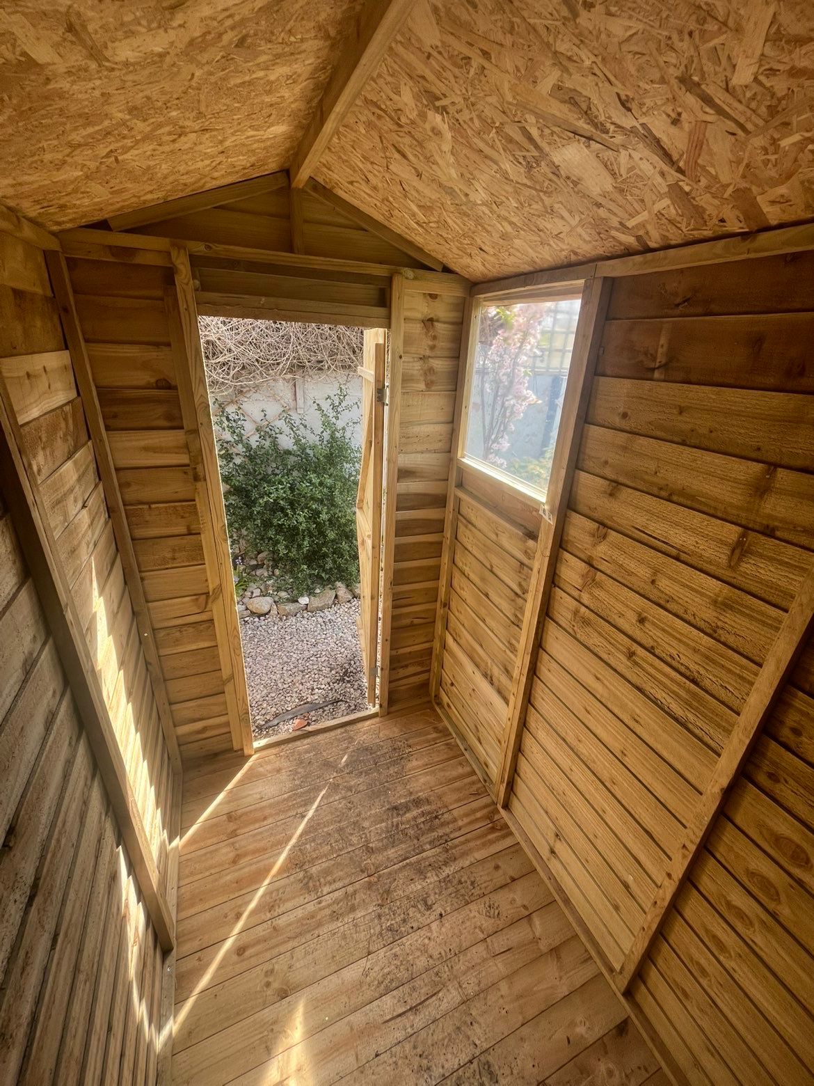 Interior of a newly built timber shed showing boarded floor, side window and stable door opening to the garden