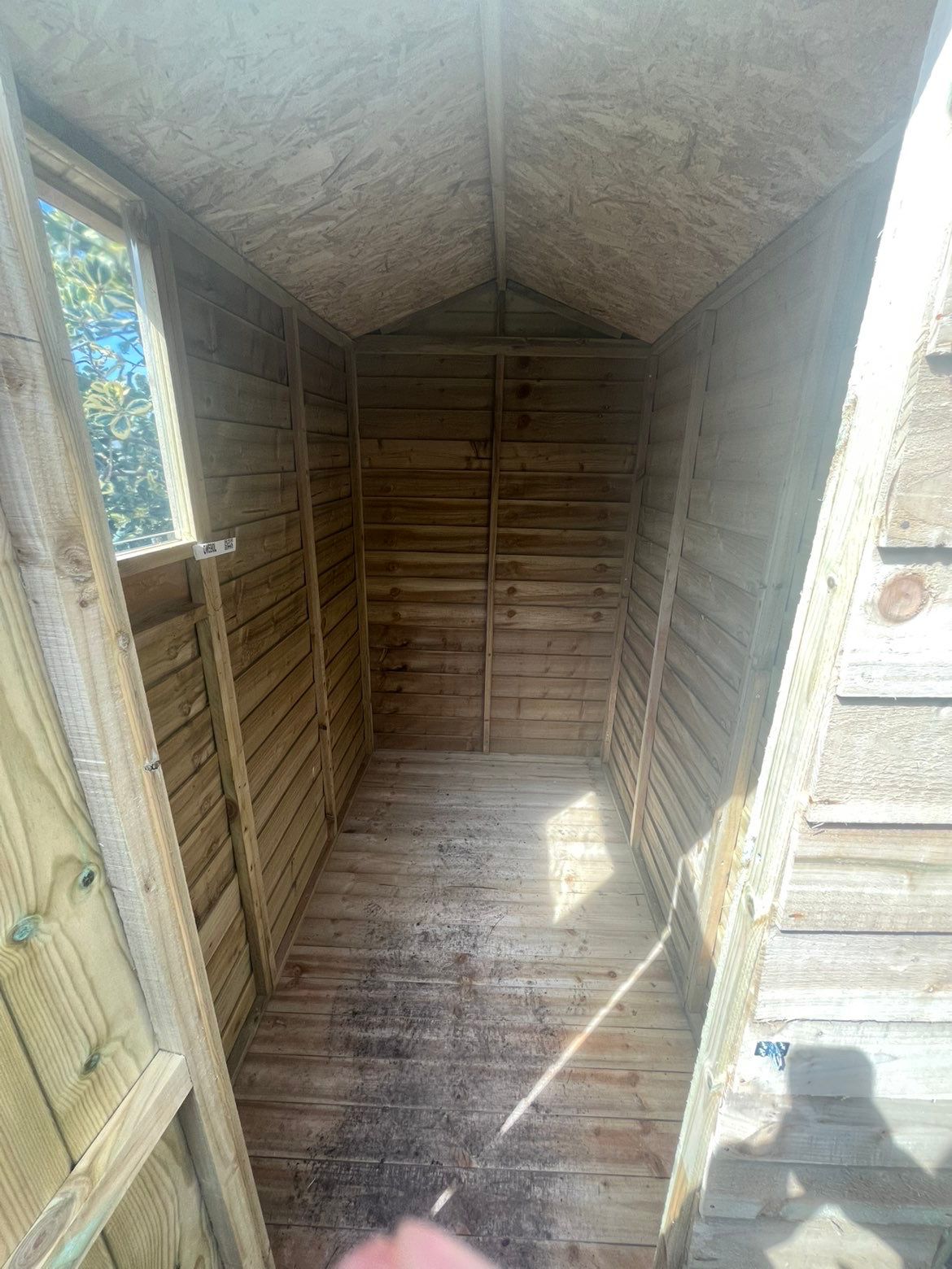 View from the shed doorway towards the rear wall, showing full timber lining, pitched roof and boarded floor