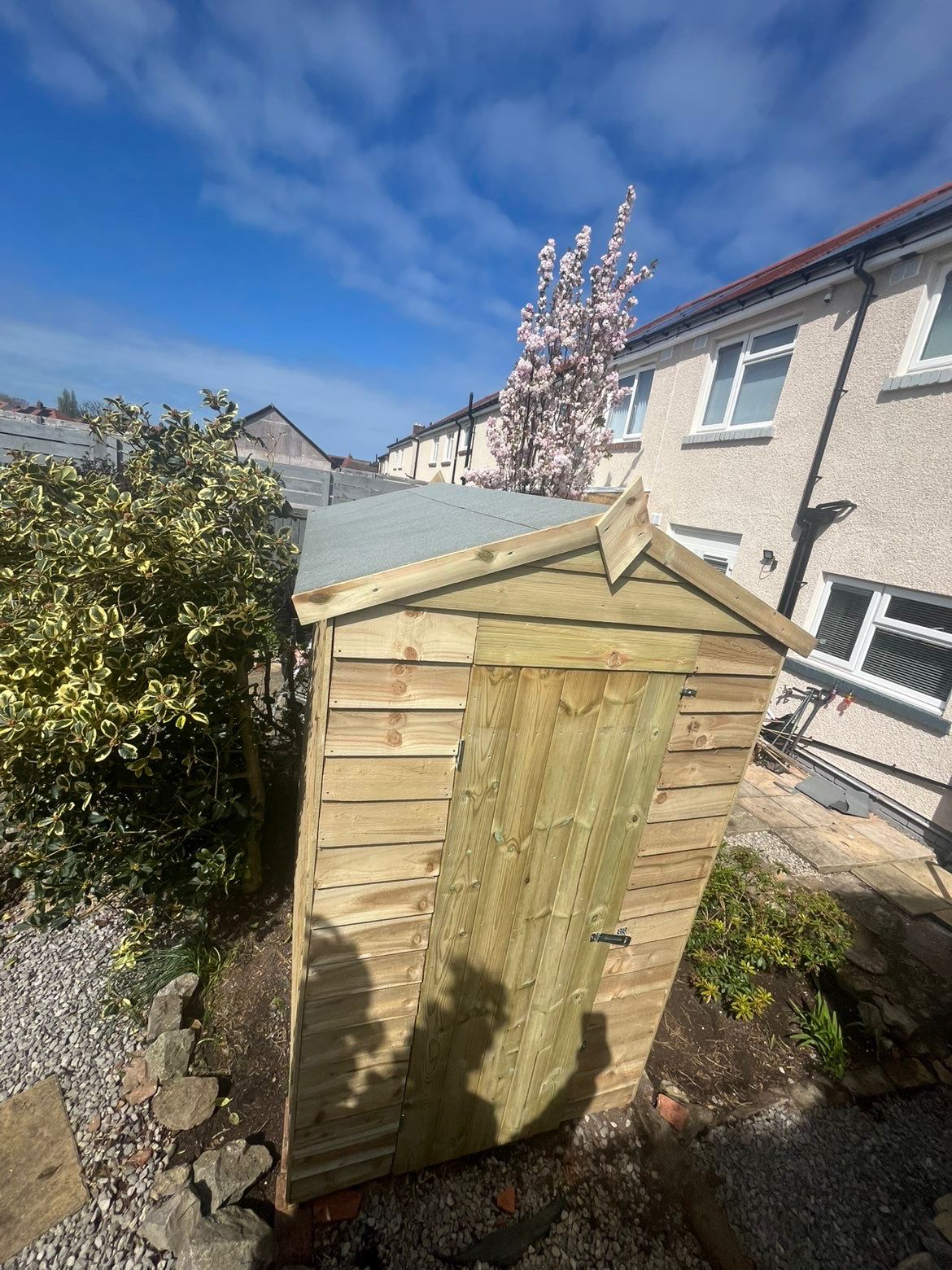 Wider exterior view of the completed timber shed in a garden setting, showing the roof, front elevation and compact footprint